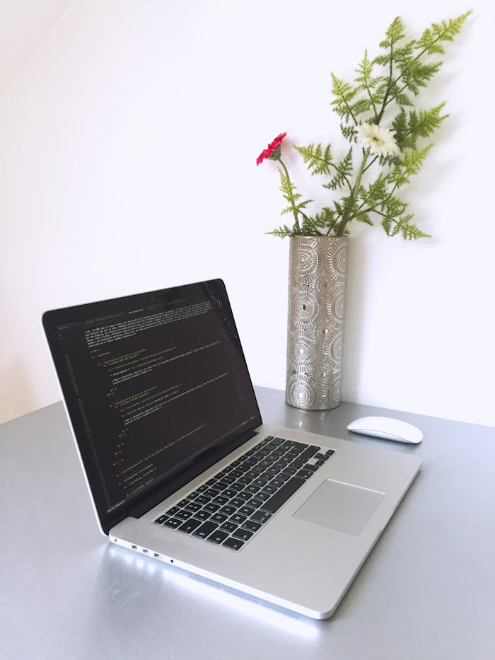 our-story Laptop with programming code on screen beside a vase with flowers, creating a modern workspace.